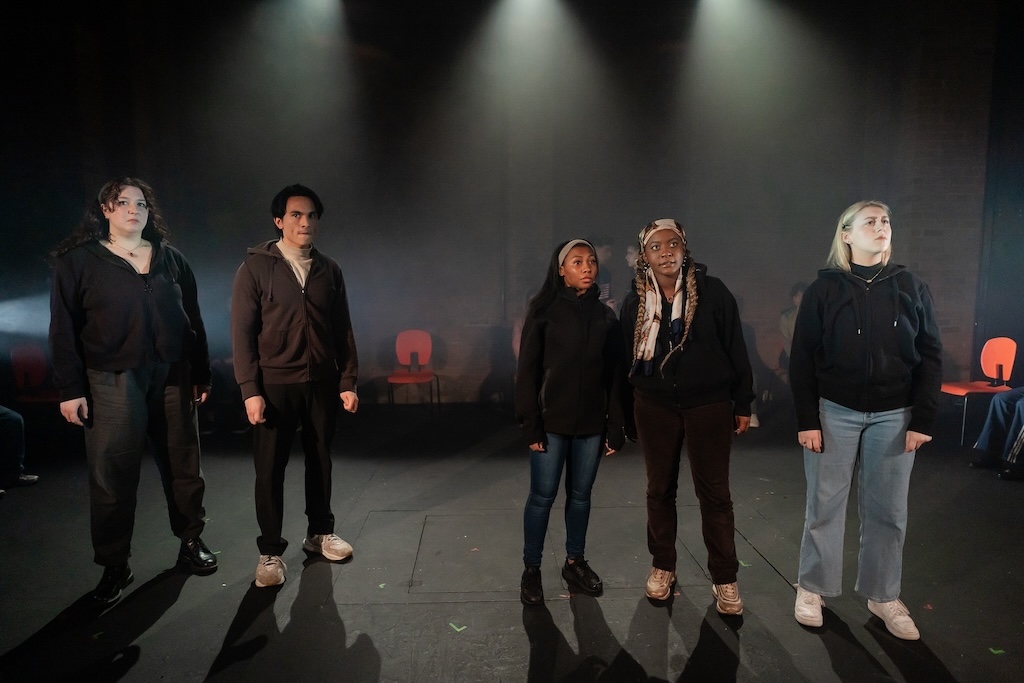 Action shot of the spring 2024 Shakespeare in Performance at RADA final presentation of Julius Caesar. Several actors stand on stage, facing the camera, with concerned expressions on their faces.